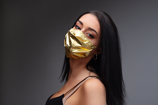 woman wearing a golden face mask - concept of surgical masks price rise when they are mandatory and as extremely rare as they are needed to mitigate the COVID19 virus pandemic spread