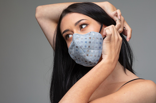 Young woman adjusting a trendy textile face mask behind her ear in a concept of adapting to a post Covid-19 fashion and lifestyle
