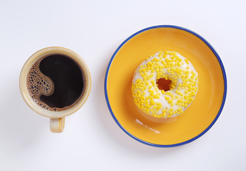 Directly above view of coffee with yellow donut on white background