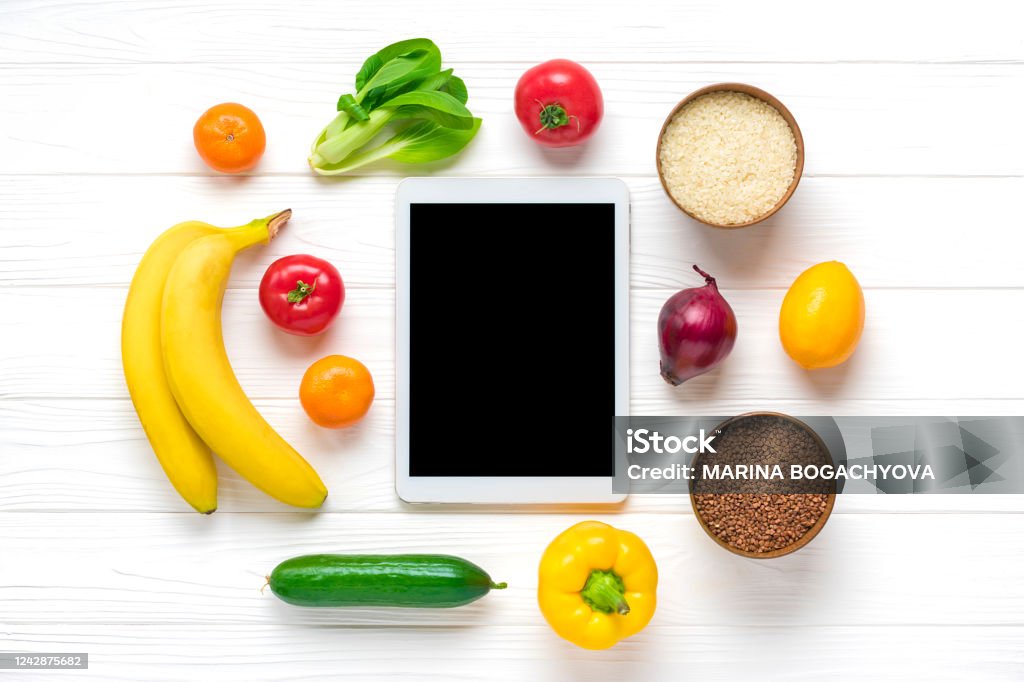 different health food - buckwheat, rice, yellow bell pepper, tomatoes, bananas, lettuce, green, cucumber, onions, tablet with black screen on white background Top view Flat lay Online shopping Mockup different health food - buckwheat, rice, yellow bell pepper, tomatoes, bananas, lettuce, green, cucumber, onions, tablet with black screen on white background Top view Flat lay Online shopping Mockup. Basket Stock Photo