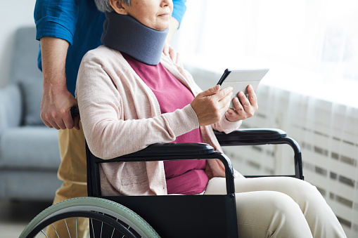 Close-up of senior woman in bandage on her neck sitting in wheelchair and using digital tablet