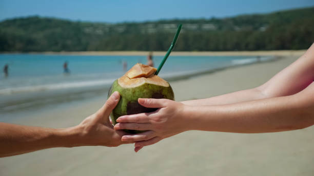 istock Man's hands pass coconut to woman's hands on the beach 1242930534