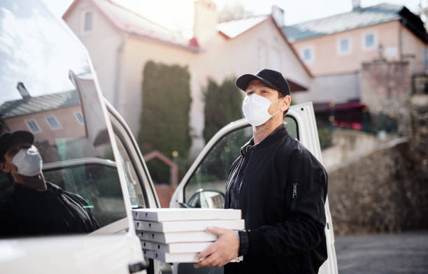 istock Delivery man courier with face mask delivering pizza in town. 1242953051