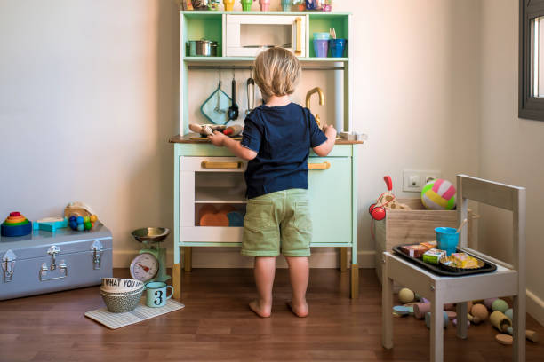 little blond boys play with a toy kitchen at home during quarantine. fun at home. family entertainment - glasses child cute offspring imagens e fotografias de stock