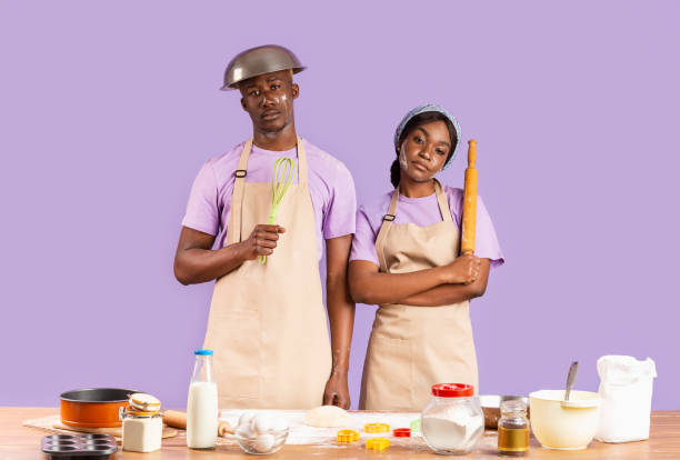 istock Exhausted black couple with kitchen utensils having hard time baking on color background 1242974609
