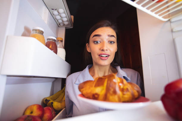 hungriges mädchen mit blick auf frisches croissant im kühlschrank - bulimia stock-fotos und bilder