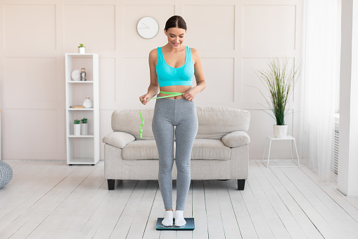 Joyful Slim Woman Measuring Waist Standing On Scales Losing Weight Slimming At Home. Full Length