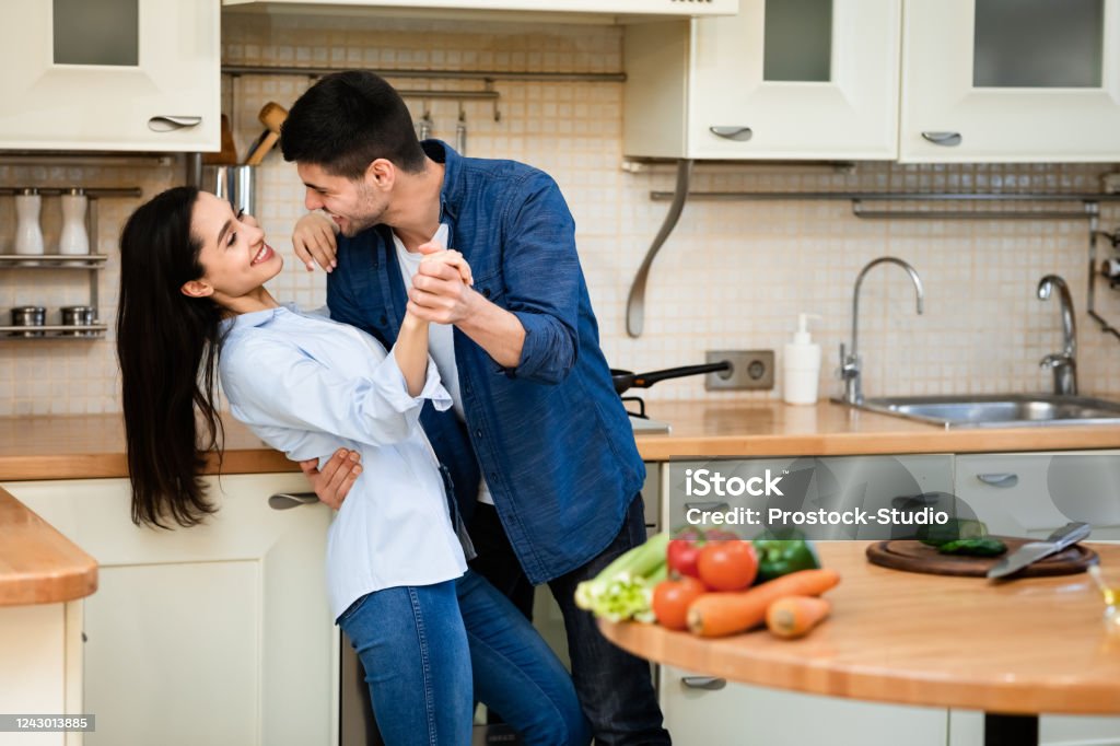 Young couple preparing dinner together at home, dancing Romantic Moments. Lovely girl and guy dancing in the kitchen, embracing, cooking healthy dinner Dancing Stock Photo
