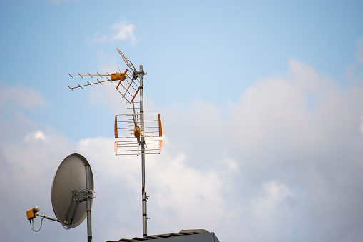 TV aerial and parabolic dish with blue sky background. Wallpaper with copy space on the right.