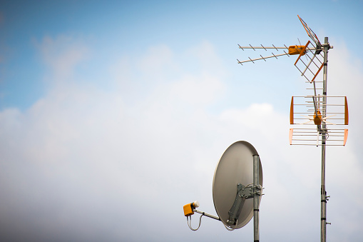 TV aerial and parabolic dish with blue sky background. Wallpaper with copy space on the left.