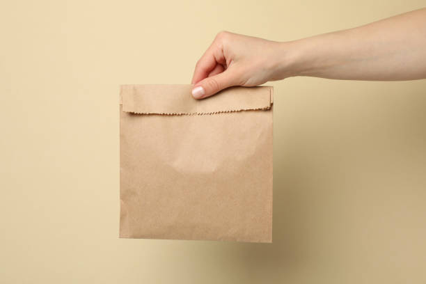 istock Female hand holding paper bag on beige background, space for text 1243019294