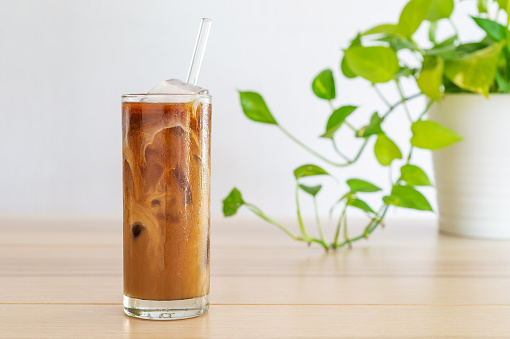 cold brew coffee with milk on white wooden table and green plant in the background.