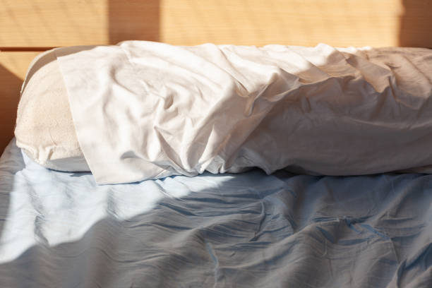istock Wake up concept: pillow on unmade bed with wrinkles on sheets lit by morning light 1243073828