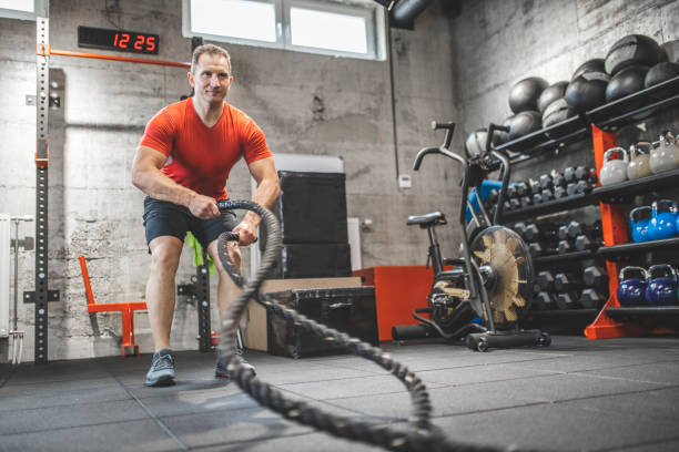 istock Athletic mid adult man doing some cross training exercises with a rope. Determined fit guy doing battle ropes exercise at the cross training gym. Handsome man training with effort 1243111914