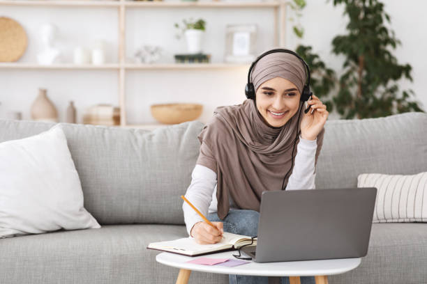 집에서 노트북으로 공부하는 머리 스카프와 헤드셋에서 미소 아랍어 소녀 - traditional clothing audio 뉴스 사진 이미지
