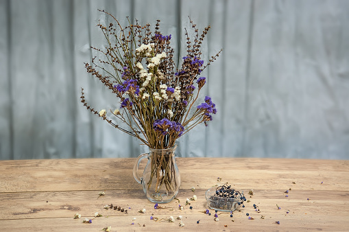 Still life of a bouquet of dried flowers in a glass jug on a wooden table.