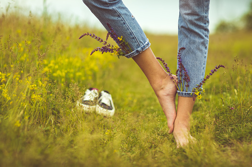 Woman leaving her shoes and walking away barefoot on green grass, closeup