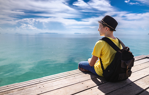 Teenager sits on wooden pier and looking forward at horizon