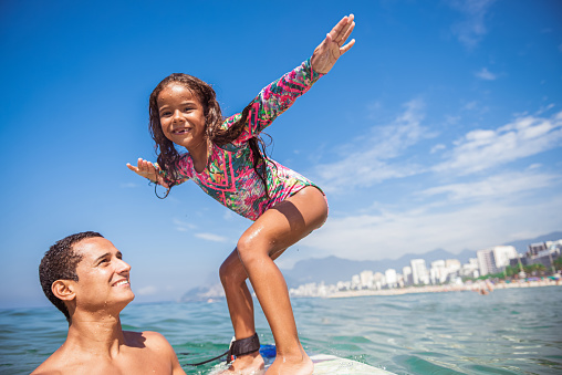 A little Brazilian girl surfing with her father