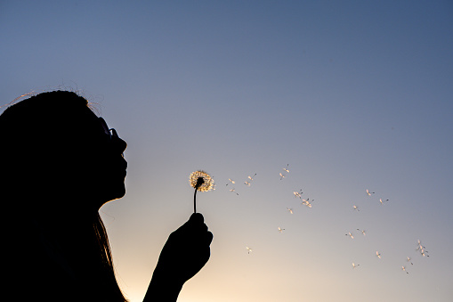 Young girl outside blowing dandelion-copy space