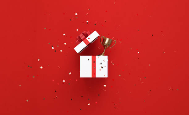 istock Star Shaped Confetti Falling Over An Open White Gift Box and Gold Trophy on Red Background 1243199093
