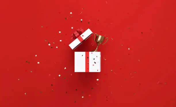 Photo of Star Shaped Confetti Falling Over An Open White Gift Box and Gold Trophy on Red Background
