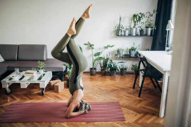 One beautiful young woman doing yoga on exercise mat in her living room, headstand pose.