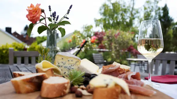 Antipasto with glass of white wine on a garden terrace. Summerly food photography with short depth of field space. Background for a mediterranean gastronomy concept. Close-up.