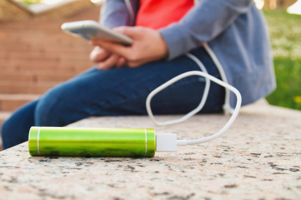 a girl uses a smartphone outdoors while charging from an external power bank - recharger imagens e fotografias de stock