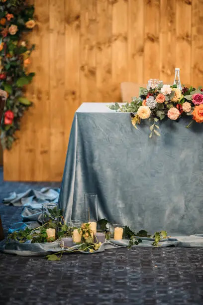 Wedding presidium in restaurant, free space. Wedding banquet table for newlyweds with flowers, greenery, blue velvet and candles . Lush floral arrangement on wedding table