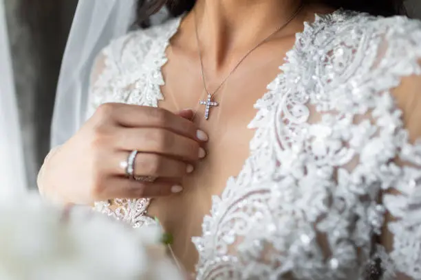 The bride's chest on which hangs a cross of white gold. Next to her hand.