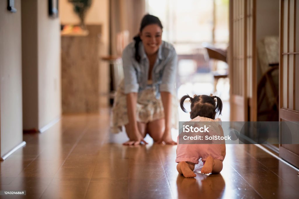 Learning to Crawl Young girl crawling along a hallway towards her mother. Life Events Stock Photo