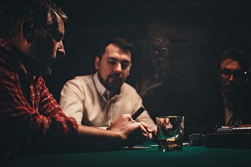 Three men, gentlemen playing poker in dark room at night.