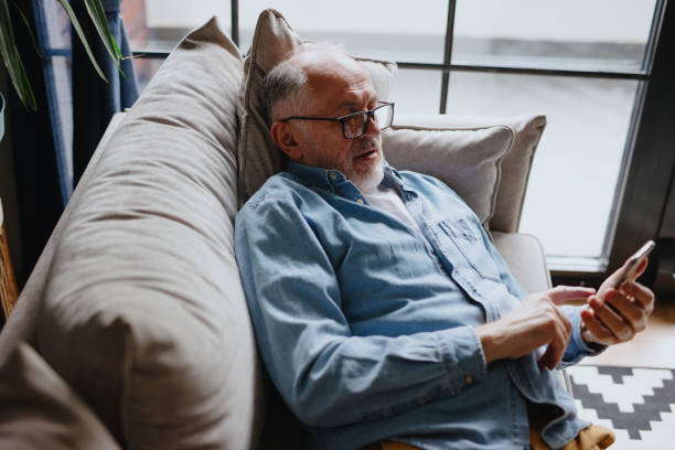 istock Mature man laying on sofa and text messaging someone on his smartphone 1243249628