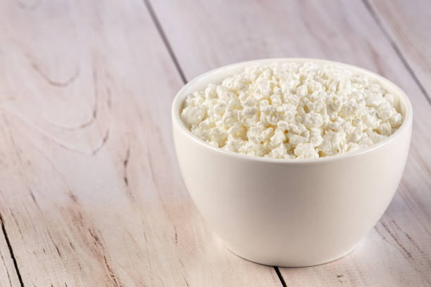 istock Natural cottage cheese or curd in a white ceramic bowl on a wooden background 1243272821