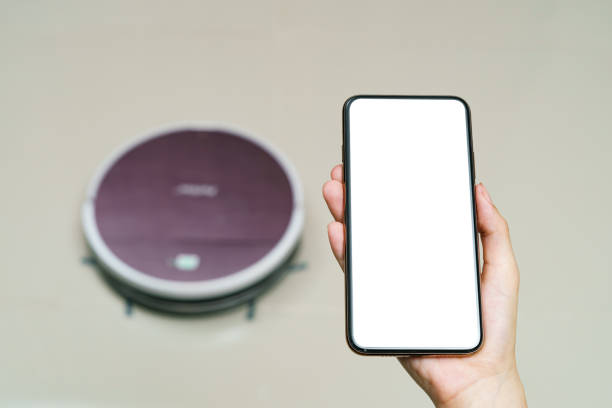 istock Hand holding smartphone with blanking screen for control robotic vacuum cleaner . Smart life technology concepts. 1243276151
