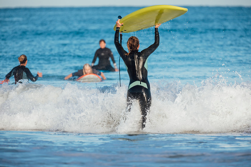 Young caucasian woman holding her surfboard above her head, running out into the water.