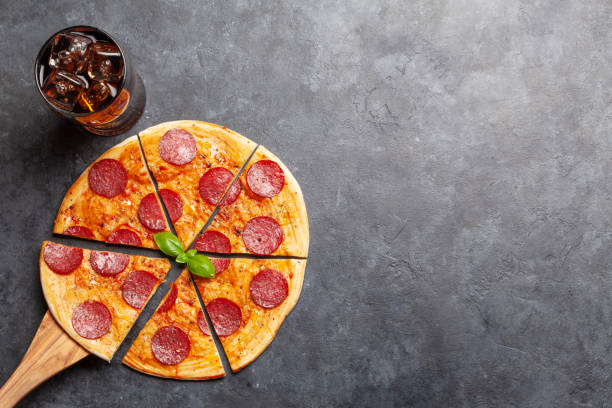 Tasty homemade pizza with pepperoni and glass of cola with ice. Top view with copy space. Flat lay