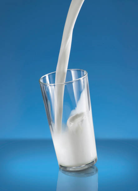 istock Pouring Milk Splash in A Glass Over Blue Background 1243342061