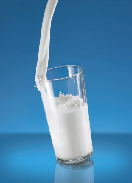 istock Pouring Milk Splash in A Glass Over Blue Background 1243344618