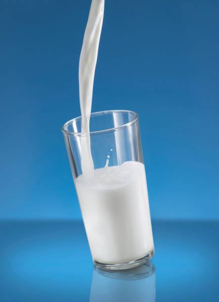 Pouring Milk Splash in A Glass Over Blue Background stock photo