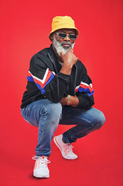 They say they like my style Studio shot of a senior man wearing retro attire while posing against a red background bucket hat stock pictures, royalty-free photos & images