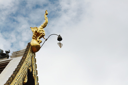 Golden naga and bells hanging on Art Roof of Buddhist temple with blue sky in Thailand