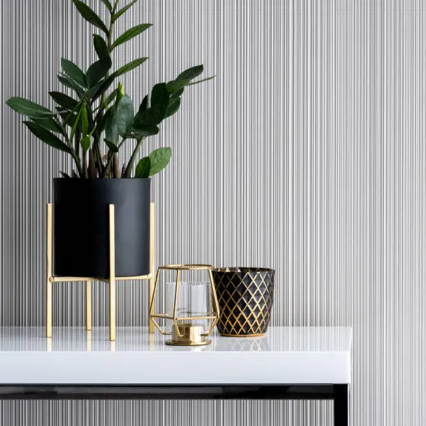 Close-up on stylish decorations in gold and black on white, high gloss console table with striped wallpaper in the background