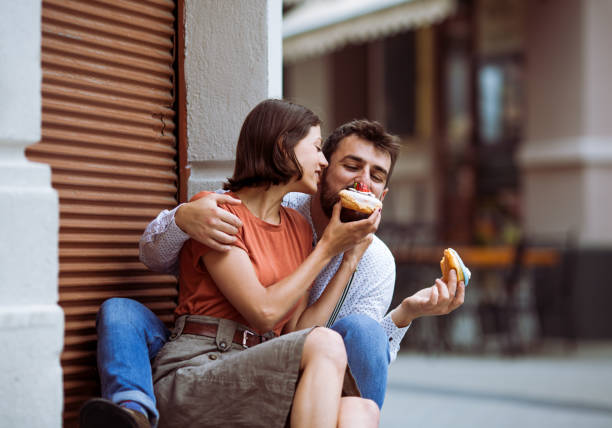 Couple eating doughnuts on street.