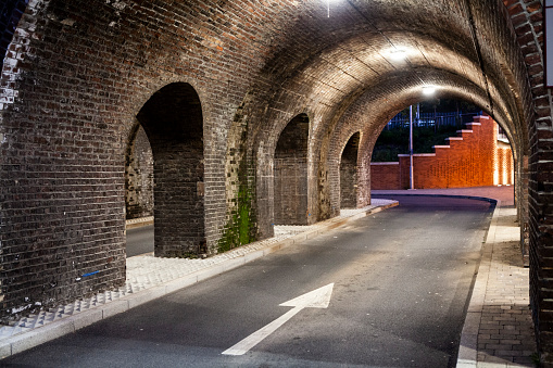Illuminated brickwork of a deserted railway arch at night with an arrow painted on the road