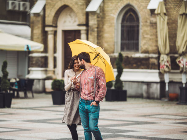 People walking on a rainy city street, one holding a red umbrella and the other a black umbrella.