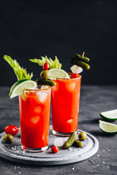 Bloody Mary Cocktail in glasses with garnishes. Tomato Bloody Mary ice cold drink with fresh celery, pickles and lime Bloody Mary Cocktail in glasses with garnishes. Tomato Bloody Mary ice cold drink with fresh celery, pickles and lime on dark background, copy space. bloody mary stock pictures, royalty-free photos & images