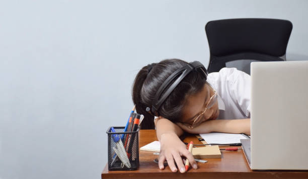 morbida attenzione al giovane studente che dorme con le cuffie sulla scrivania a casa, stanco di studiare online. - sleeping high school desk education foto e immagini stock