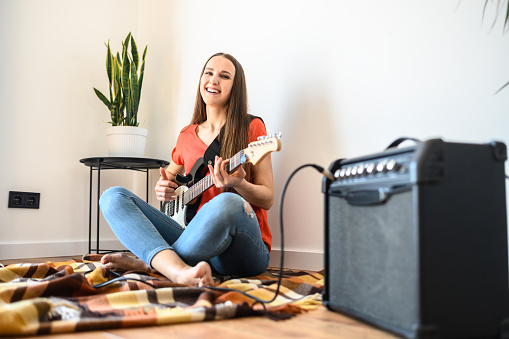 A young woman is playing an electric guitar at home using a combo amplifier. Leisure at home during quarantine, stay home
